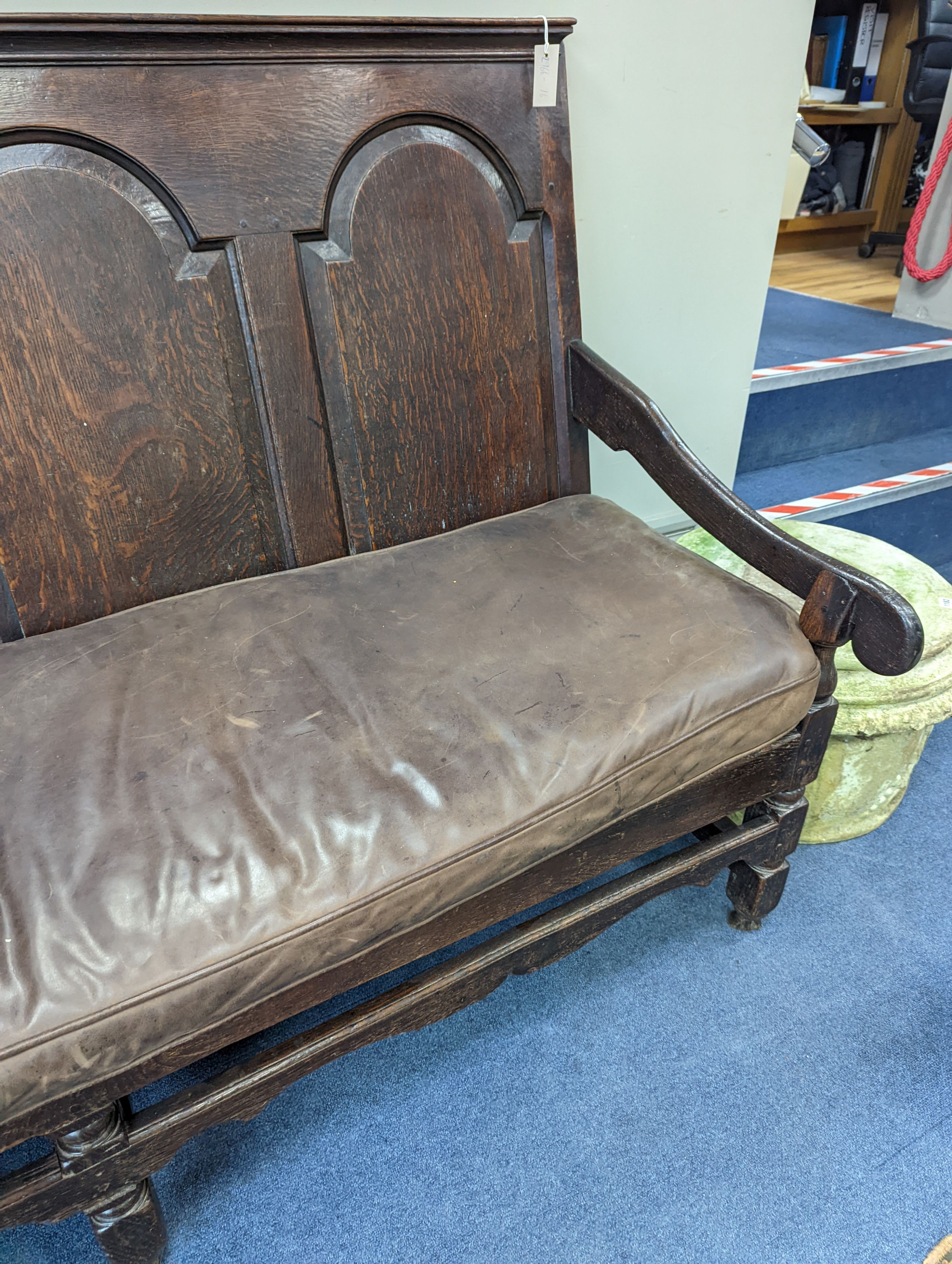 A mid 18th century panelled oak settle with leather squab seat, length 185cm, depth 77cm, height 114cm